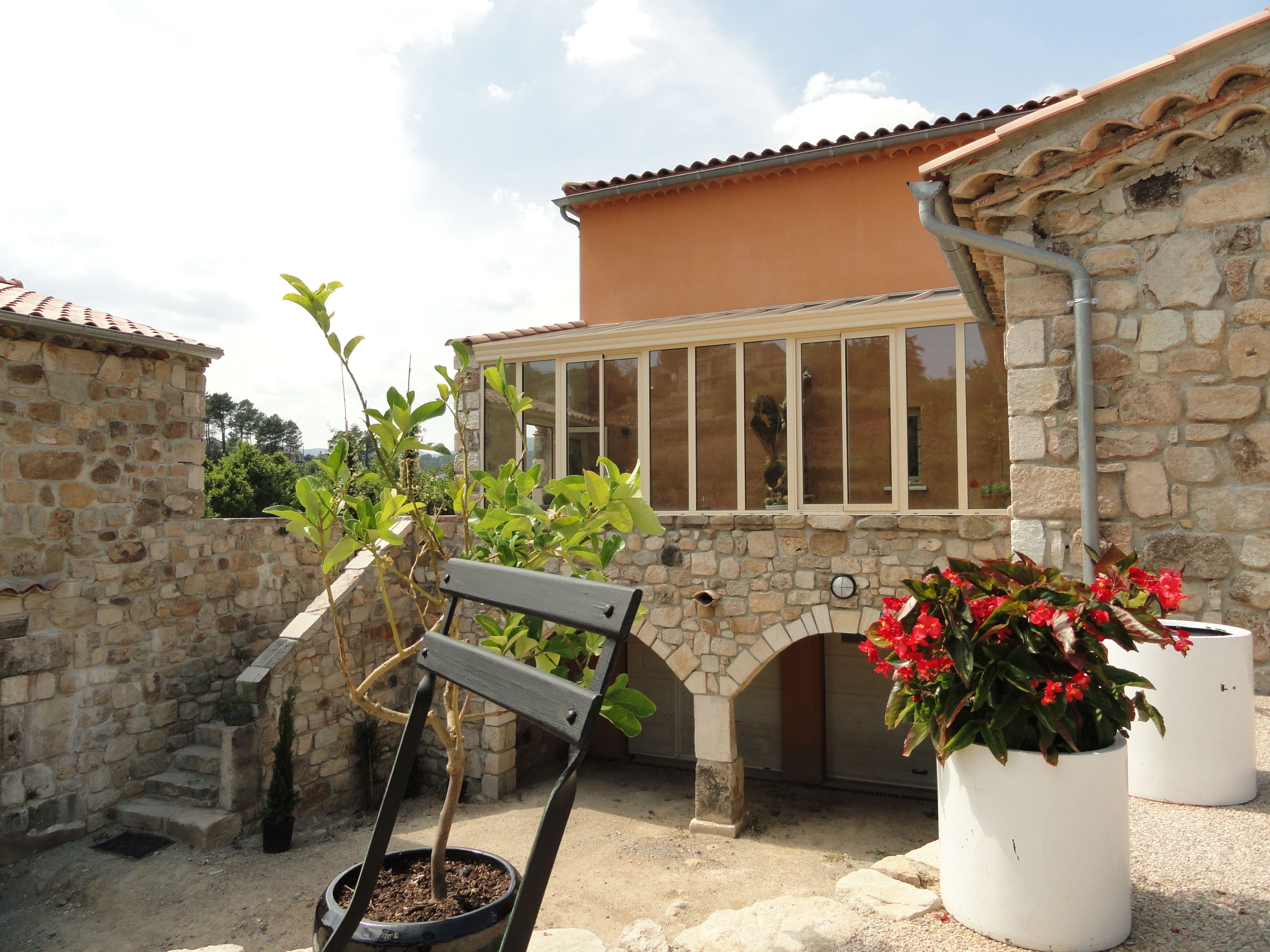 A stone building with a tiled roof, a wooden bench, and potted plants.