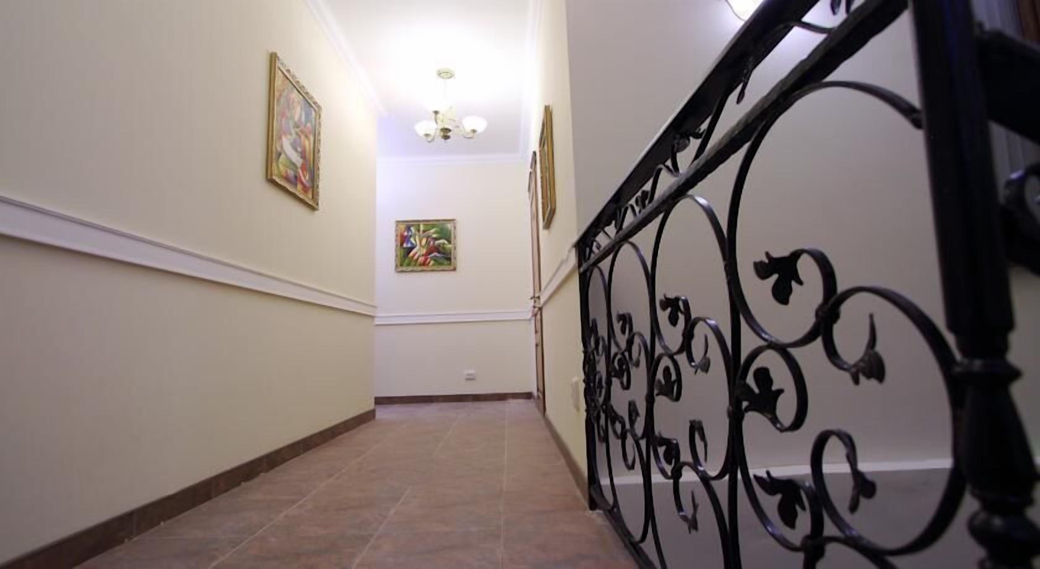 A hallway with tiled flooring, a staircase with ornate black metal railings, and two framed artworks on the walls.
