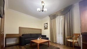 A living room with a sofa, a wooden coffee table, a chair, a headboard, and a chandelier. - Boomerang Business Hotel (Odesa)