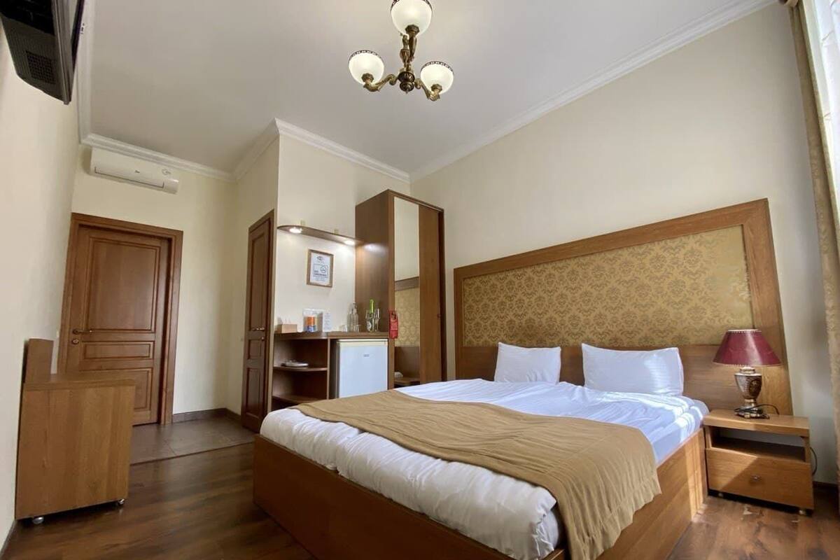 Habitación de hotel con una cama grande, cabecera de madera, mesita de noche con lámpara, armario, escritorio con silla y espejo.