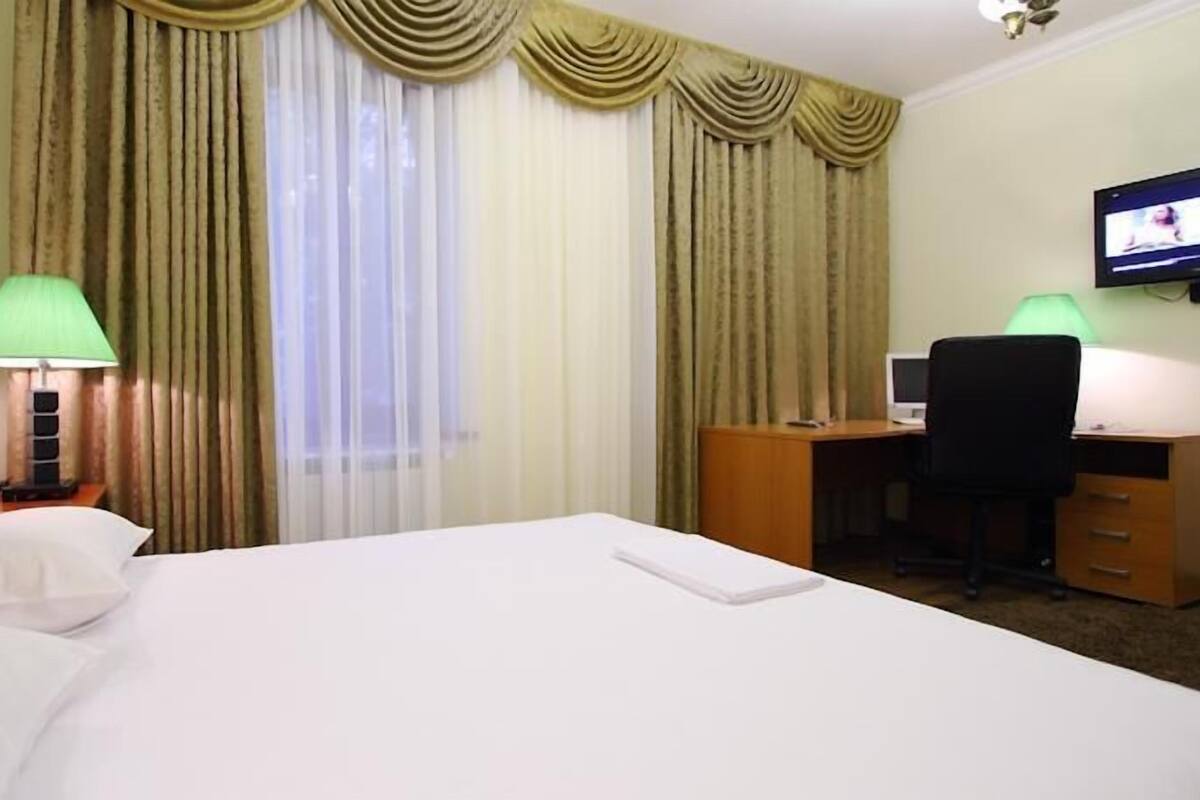 Una habitación de hotel con cama, escritorio, silla, televisor y cortinas.