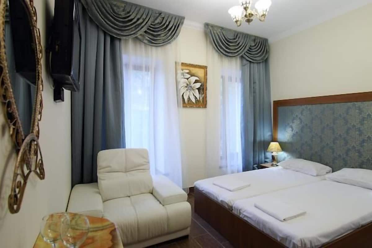 Habitación de hotel con cama doble, una silla, escritorio con lámpara y un cuadro en la pared.