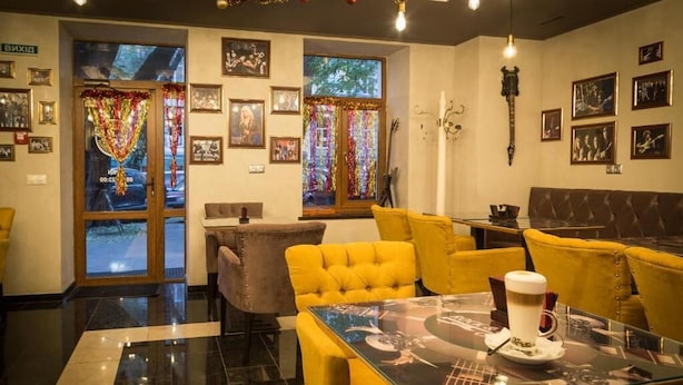 A hotel lobby with yellow seating, a glass table with a coffee cup, framed pictures on the walls, and a large window with a view. - Boomerang Business Hotel (Odesa)