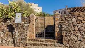 A stone wall with a metal gate, a sign for 'Albergo Castello Malgaia', and a building in the background. - Castello Malicas (Galtelli)