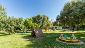 A playground with swings, slides, and a small building in the background. - Castello Malicas (Galtelli)