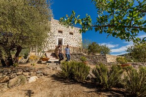 A stone building with a staircase leading to the entrance, surrounded by dry vegetation and a clear blue sky. - Castello Malicas (Galtelli)