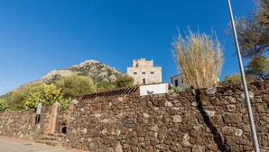 A stone wall with a staircase leading to a building with a tower. - Castello Malicas (Galtelli)