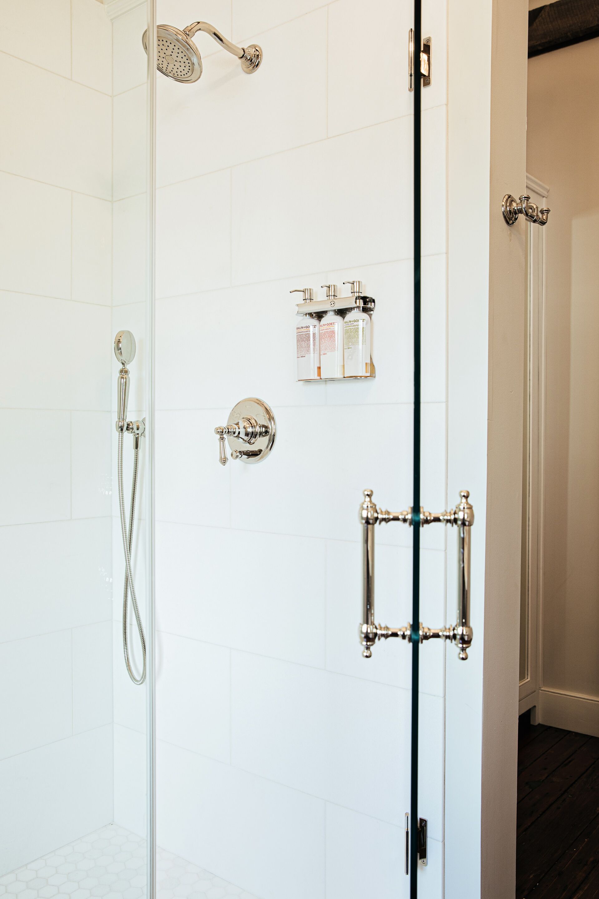 Un baño moderno con cabina de ducha de vidrio, accesorios de cromo y pared cubierta de azulejos blancos.