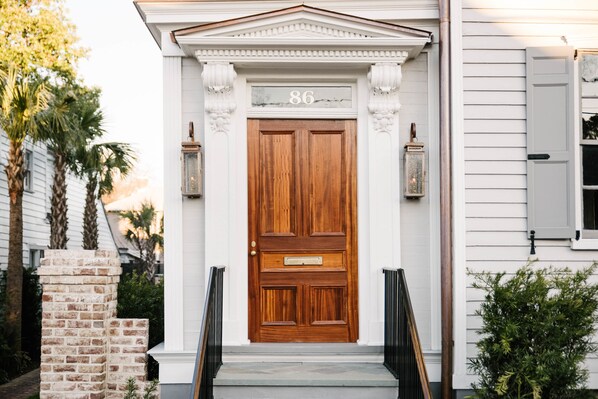 A wooden front door with a mailbox, number 86, and two wall-mounted lanterns.
