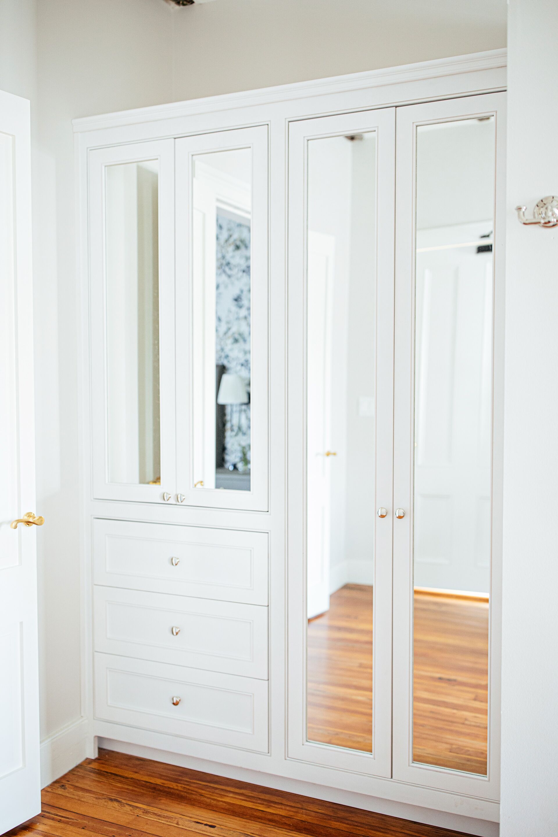 A white wardrobe with mirrored doors and a mirror above the doors.
