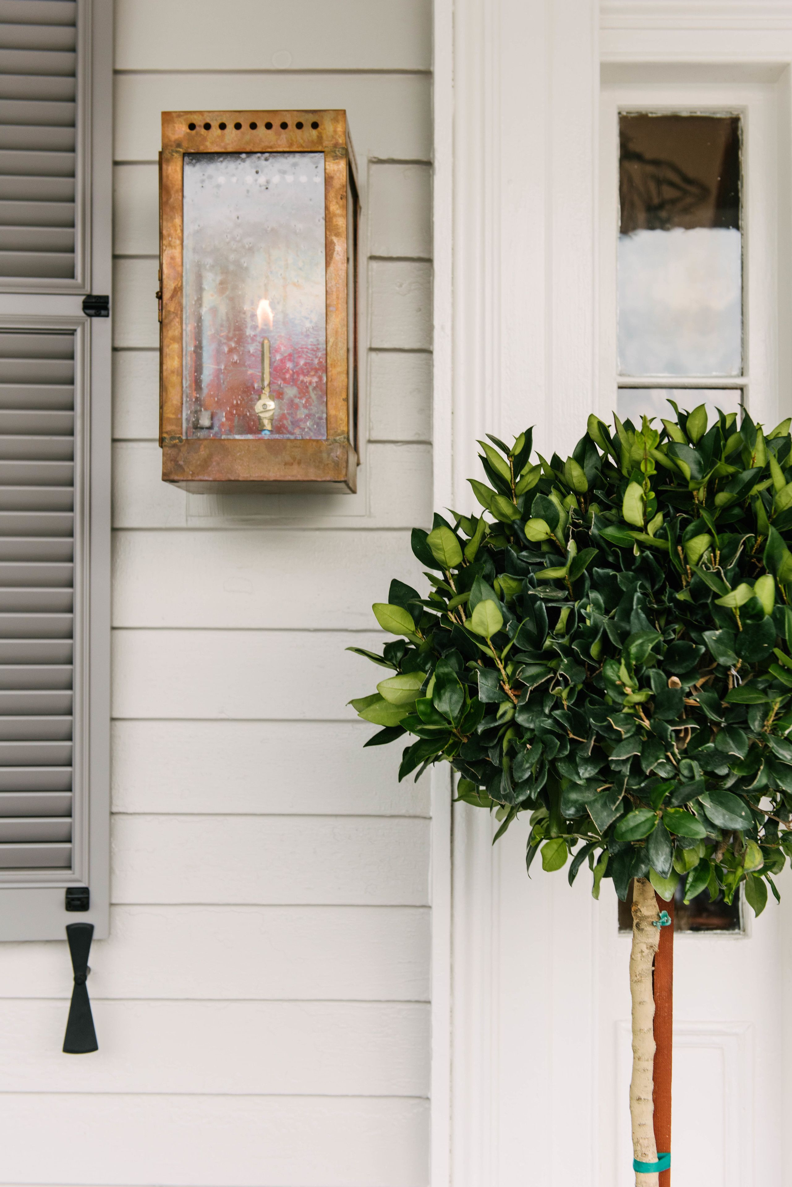 A white exterior wall with a window, a wall-mounted lantern, and a potted plant.