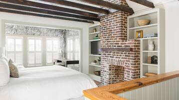A bedroom with a brick fireplace, a bed with white bedding, and a wooden headboard.