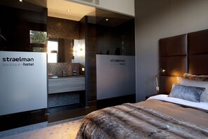 Moderni hotellihuone, jossa on suuri sänky, kylpyhuone peilillä ja pesualtaalla sekä kyltti, jossa lukee: ”Straelman Boutique Hotel”.