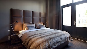 Un dormitorio moderno con una cama grande, una mesita de noche, una lámpara y vistas al exterior a través de un ventanal amplio.