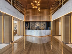 A modern reception area with a marble reception desk, a decorative ceiling, and a polished floor.