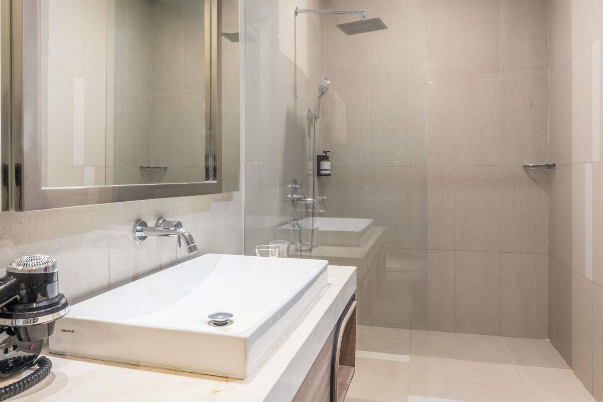 A modern bathroom with a large mirror, a sink, a shower, and a toilet.