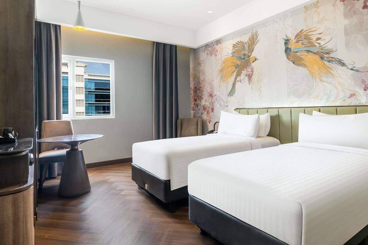 A hotel room with two beds, a dining table, a chair, a sofa, a window with blinds, and a wall with a bird mural.