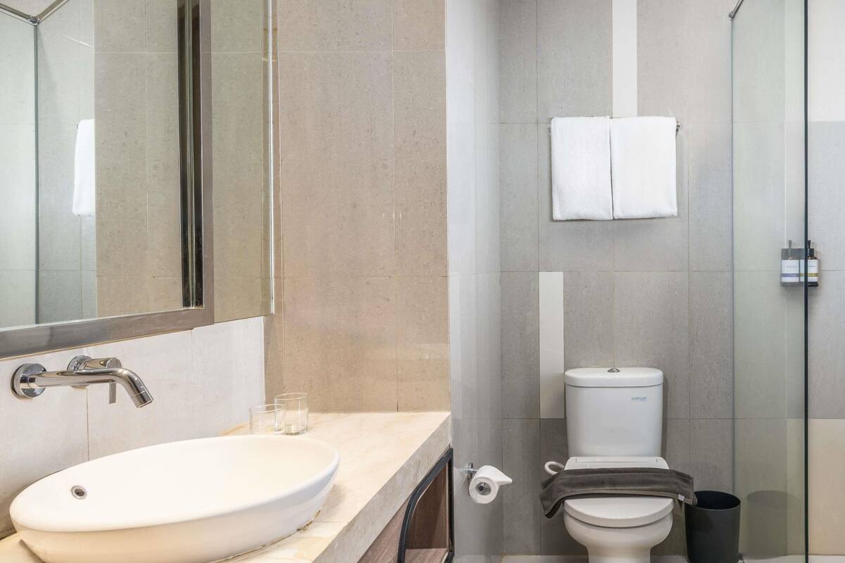 A modern bathroom with a large oval sink, a toilet, and a glass shower enclosure.