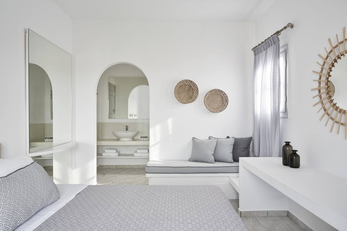 Une chambre moderne comprenant un lit, une coiffeuse avec un miroir, un banc avec des coussins et un élément décoratif fixé au mur.