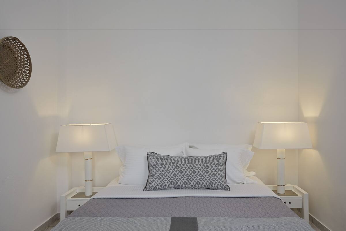 Un lit bien fait, avec deux lampes de chevet, un coussin à motifs et un objet décoratif fixé au mur.