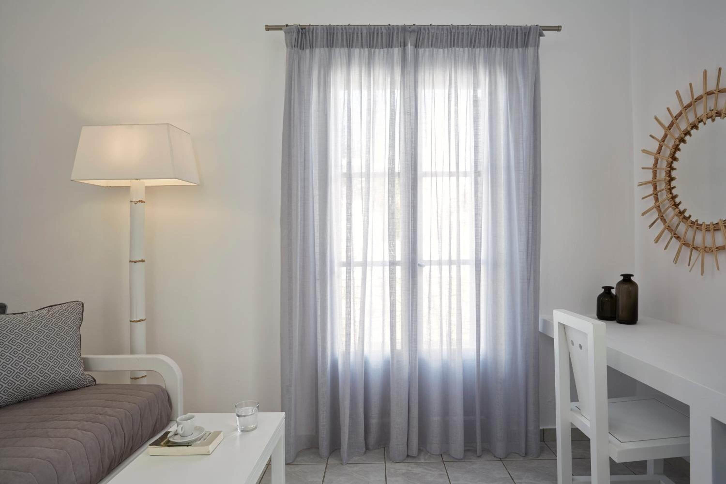 A bedroom with a bed, bedside table, lamp, and a window with sheer curtains.