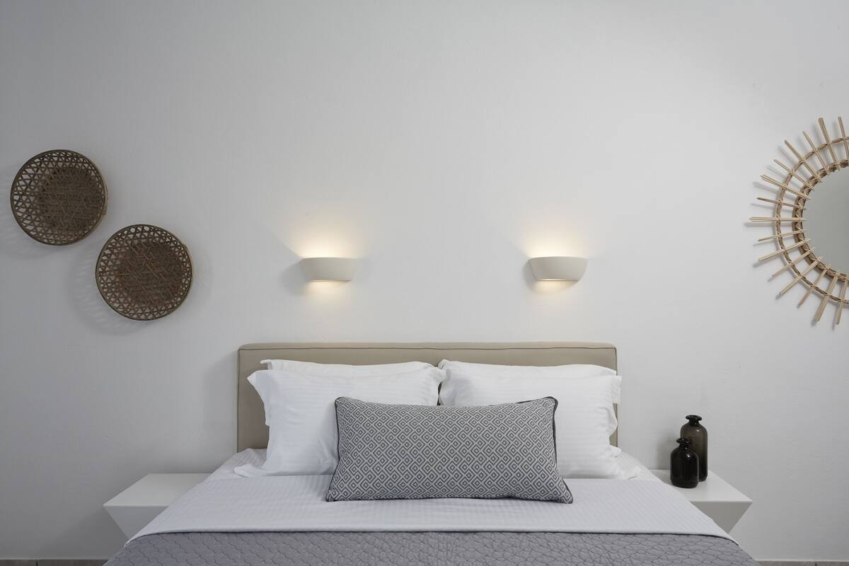 Un lit bien fait, agrémenté d’un coussin à motifs, de deux appliques murales et de deux éléments décoratifs suspendus au mur.
