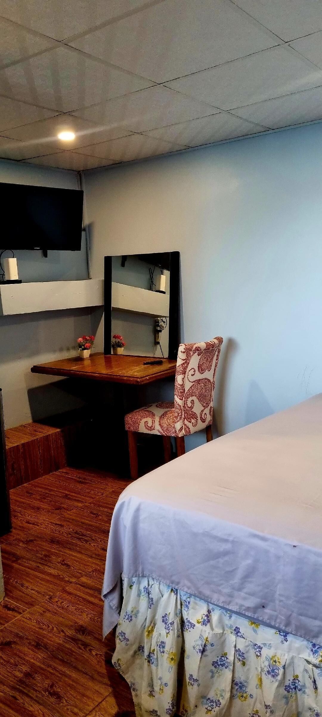 A hotel room with a bed, a desk, a chair, a TV, and a mirror.
