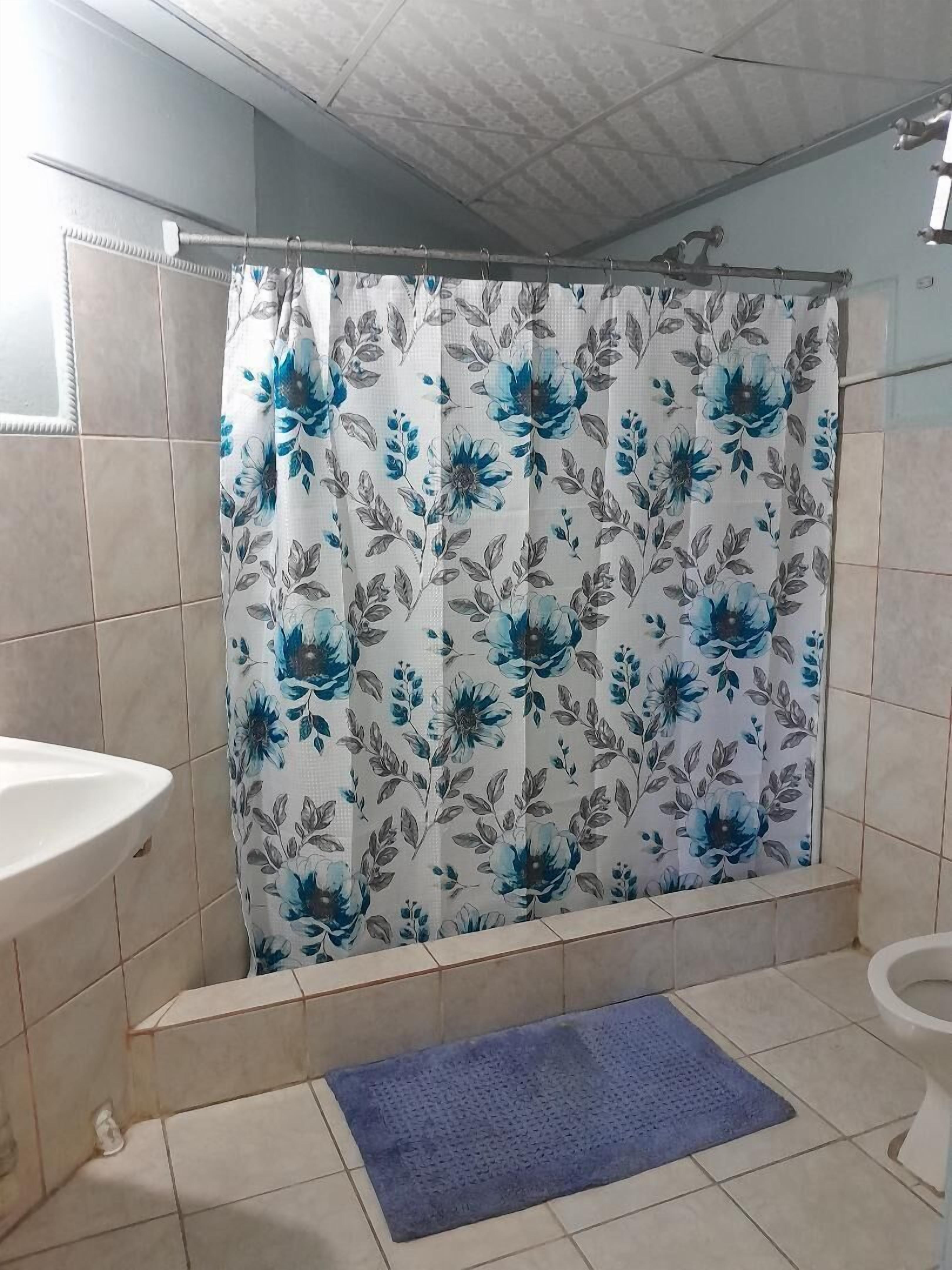 A bathroom with a shower curtain featuring a blue floral pattern, a white sink, and a blue mat on the floor.