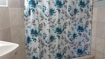 A bathroom with a shower curtain featuring a blue floral pattern, a white sink, and a blue mat on the floor.