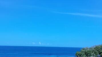 Vista costera con cielo azul despejado, mar tranquilo y una pequeña isla con vegetación.
