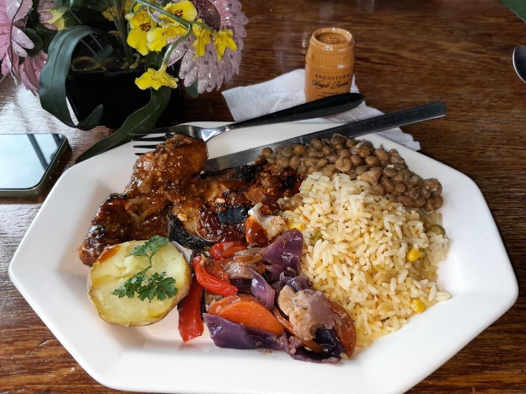 Un plato de comida con arroz, frijoles, carne y verduras sobre una mesa.