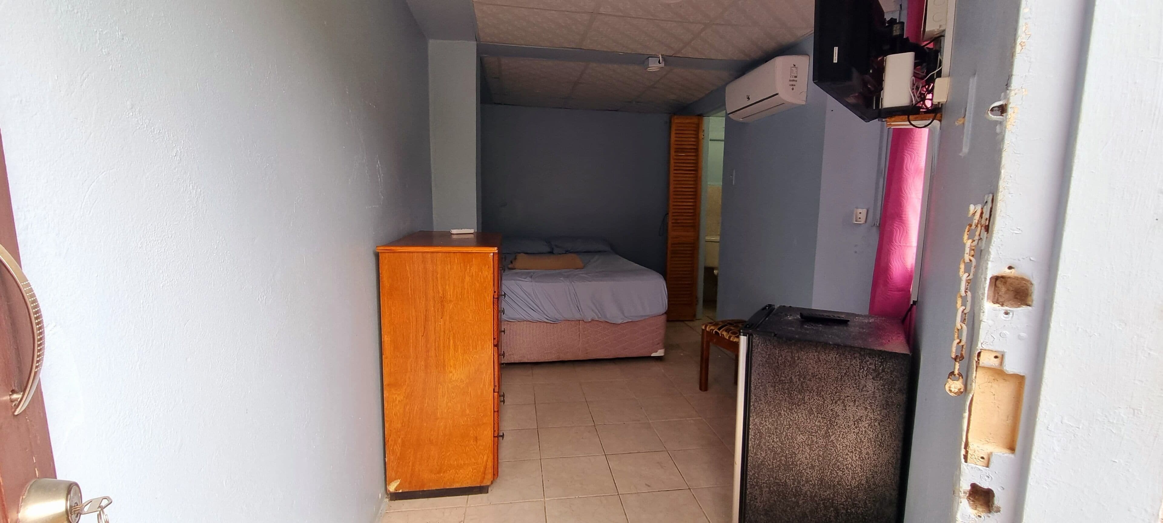 A small, compact room with a bed, a wooden dresser, and a small table.