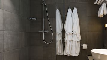 Un baño moderno con ducha de vidrio, un lavamanos grande y dos toallas blancas colgadas en ganchos.