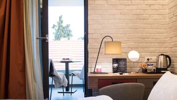 Habitación de hotel con cama, escritorio con lámpara, cafetera y vistas al exterior.