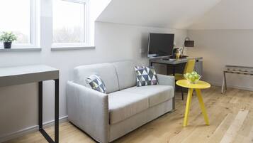 Ein modernes Wohnzimmer mit einem grauen Sofa, einem kleinen gelben Tisch mit Äpfeln, einem Fernseher auf einem Schrank und einem Fenster mit einer Pflanze.