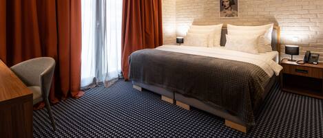 Habitación de hotel con una cama grande, una silla, una mesita de noche con lámpara y una pared de ladrillo.