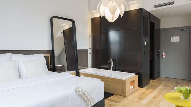 A modern hotel room with a large bed, a bathroom with a bathtub, a mirror, and a small table with apples. - Livris Hotel (Zagreb)