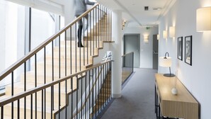 A modern hotel corridor with a wooden staircase, a reception desk, and framed artwork on the walls. - Livris Hotel (Zagreb)