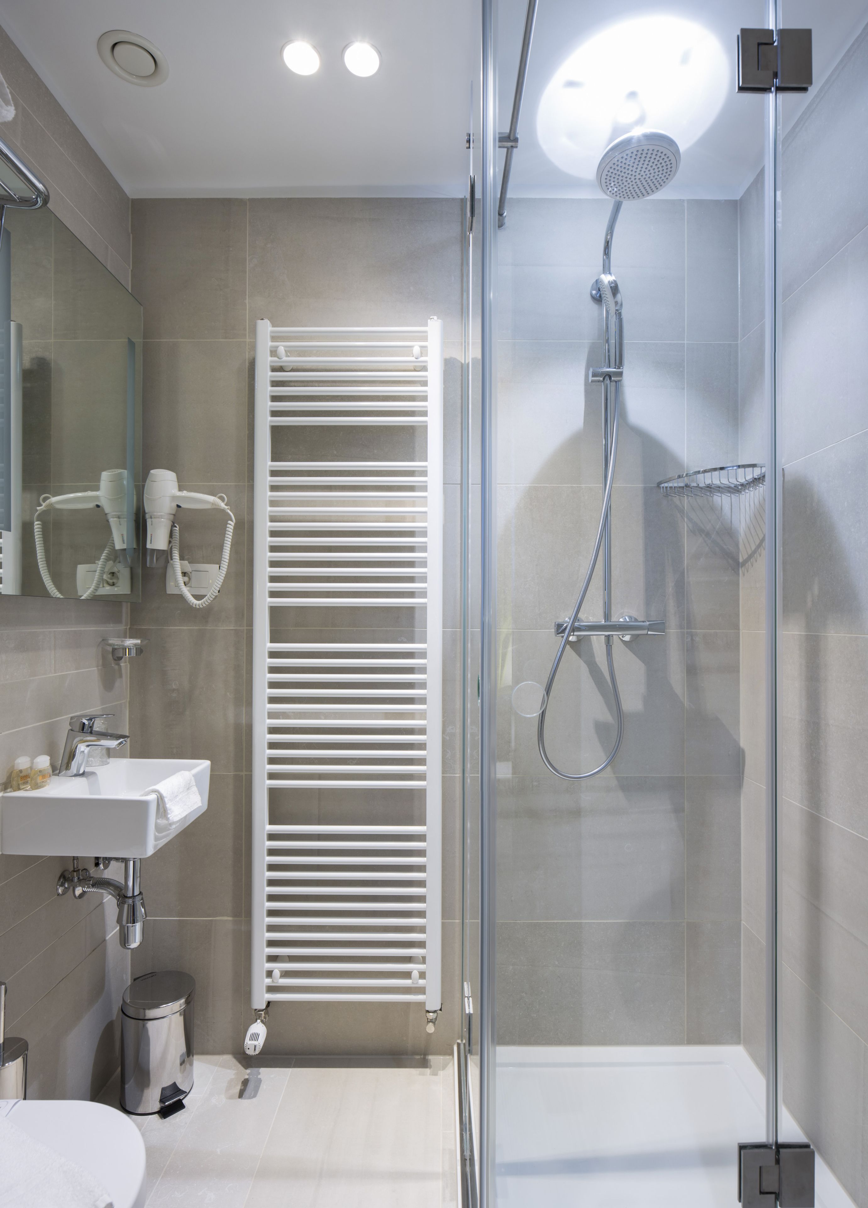 Un baño moderno con ducha envuelta en vidrio, toallero blanco y lavamanos integrado.