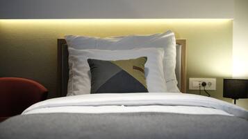 Een net opgemaakt bed met witte lakens en een sierkussen met een geometrisch patroon.