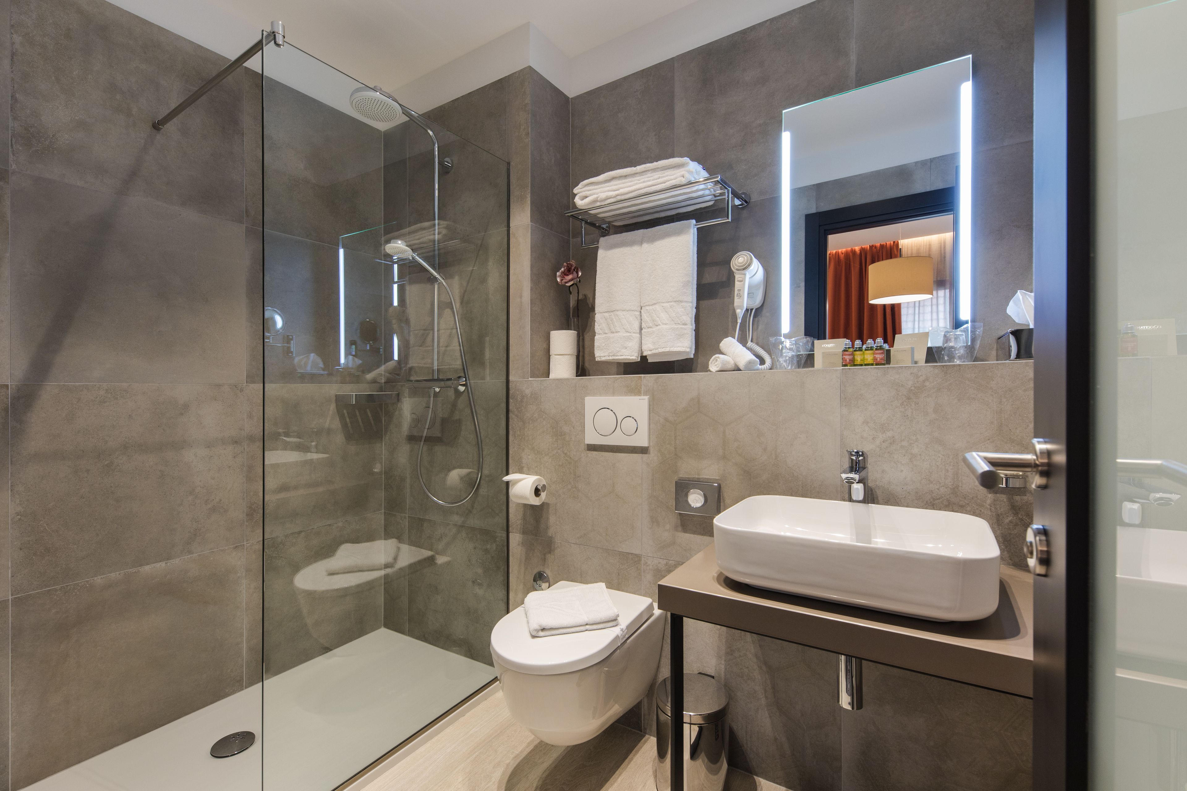 A modern bathroom with a glass-enclosed shower, a toilet, a sink, and a mirror.
