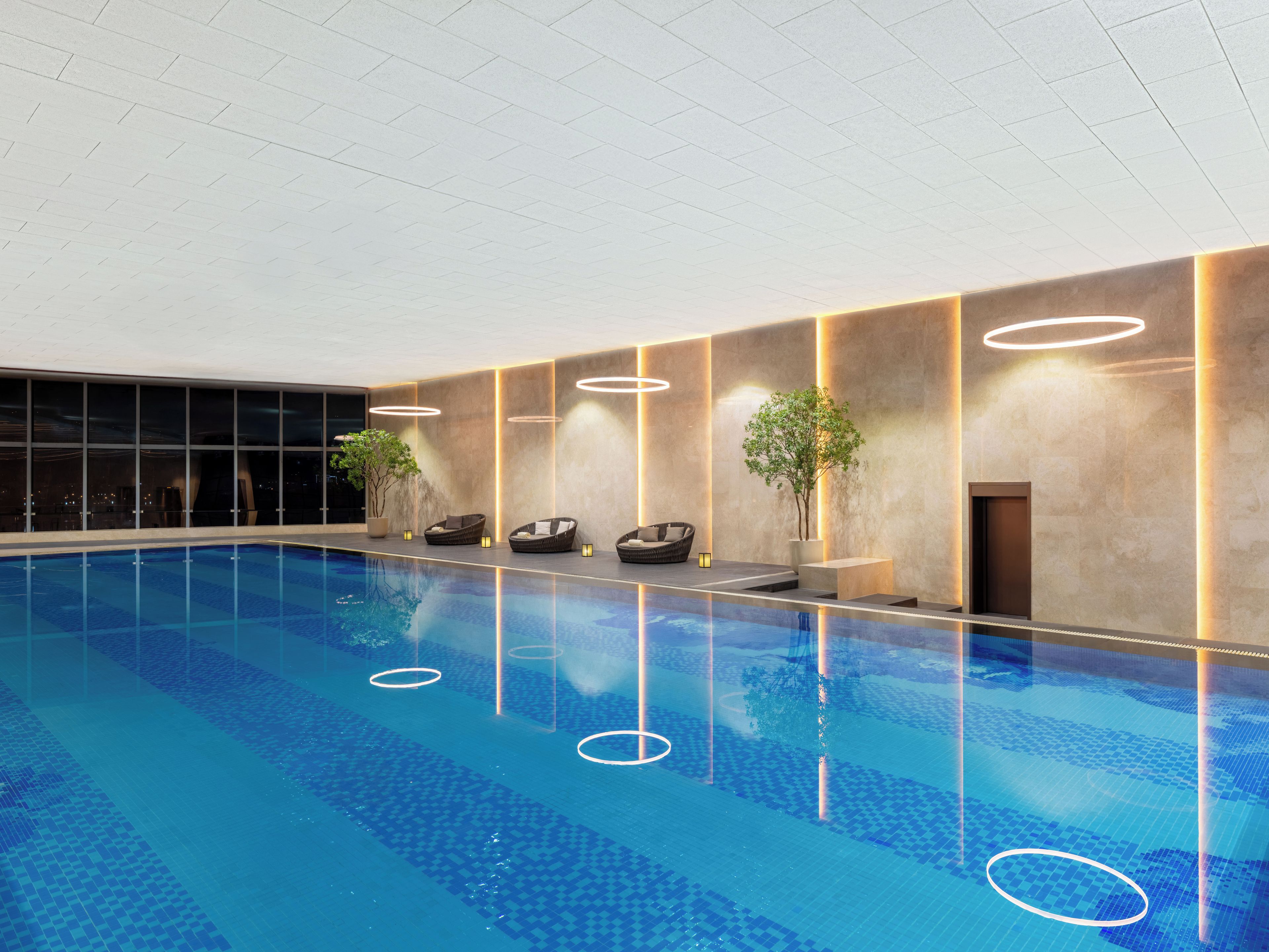 En indendørs swimmingpool med flisegulv, liggestole og en potteplante.