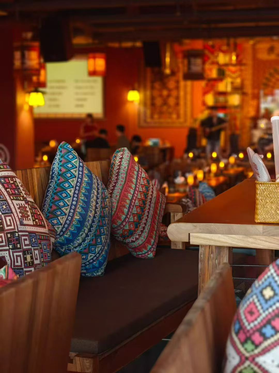 Un interior de restaurante con bancos de madera y cojines de colores con estampados.