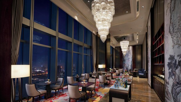 Een hoog hotel met een ruime lobby, grote ramen, kroonluchters en een traditionele Chinese muurdecoratie.