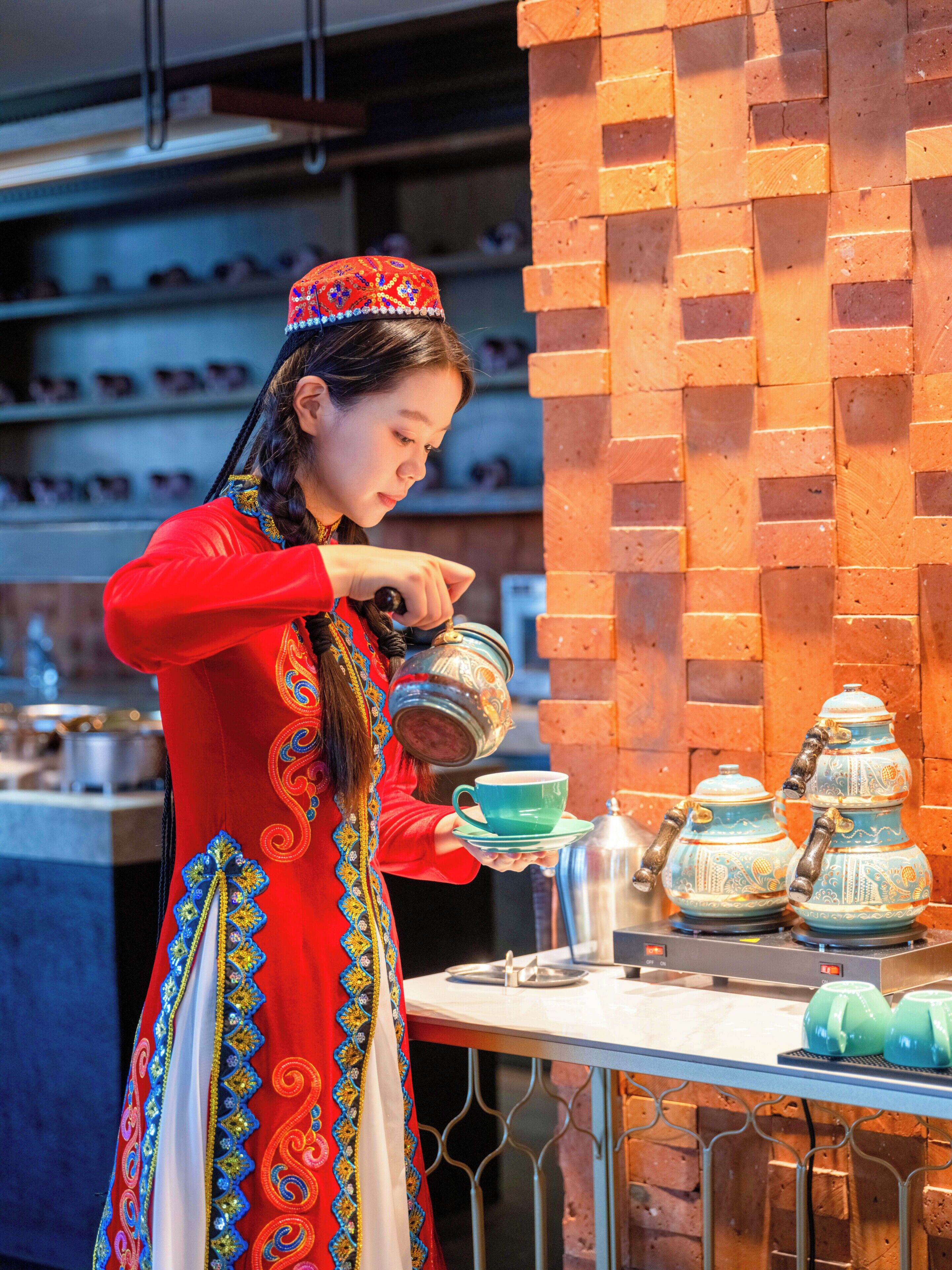 Une personne vêtue d’un costume traditionnel sert du thé, en le versant d’une théière dans une tasse.