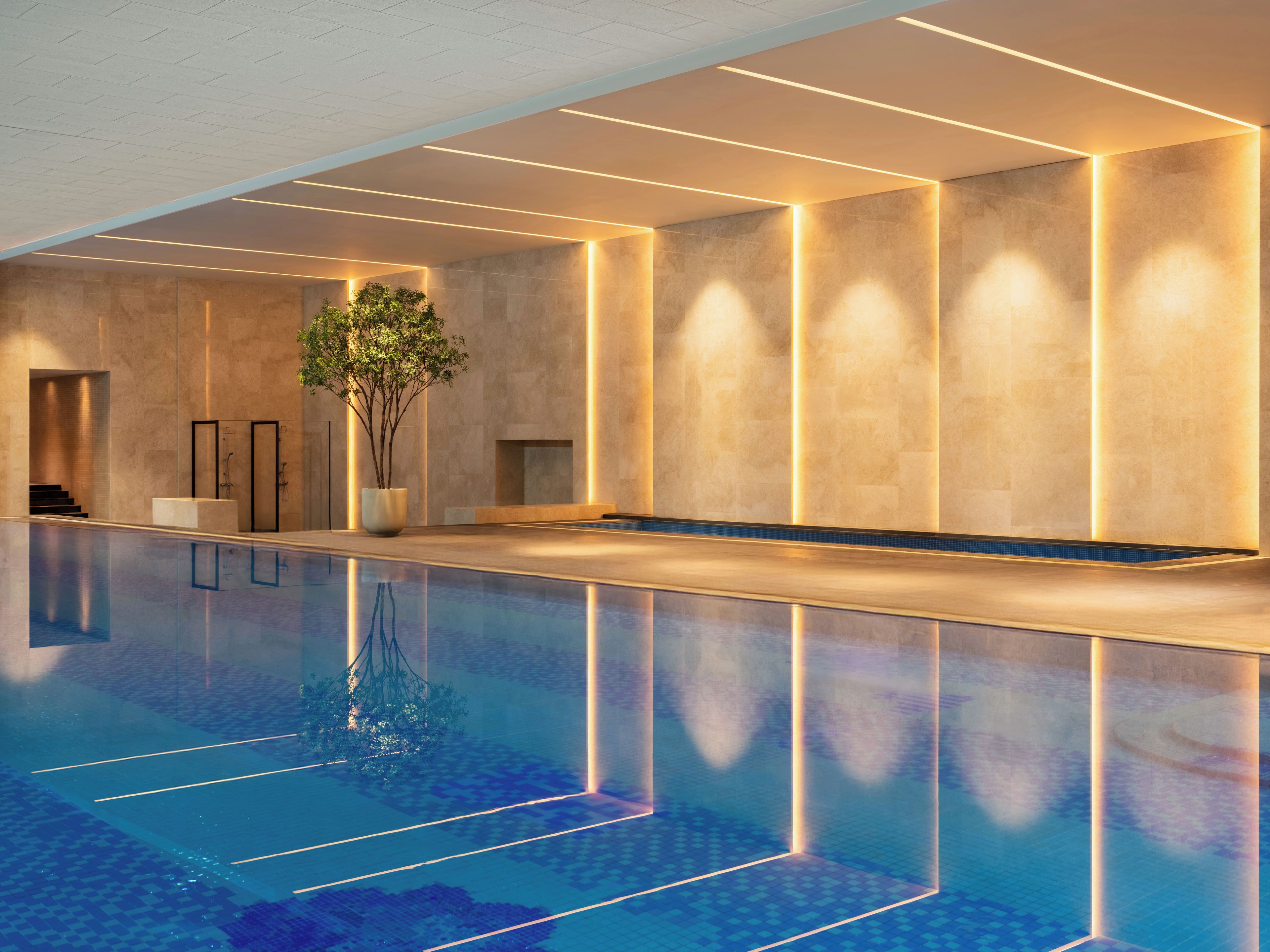 Una piscina interior moderna con superficie de agua cristalina, rodeada de paredes con iluminación integrada.