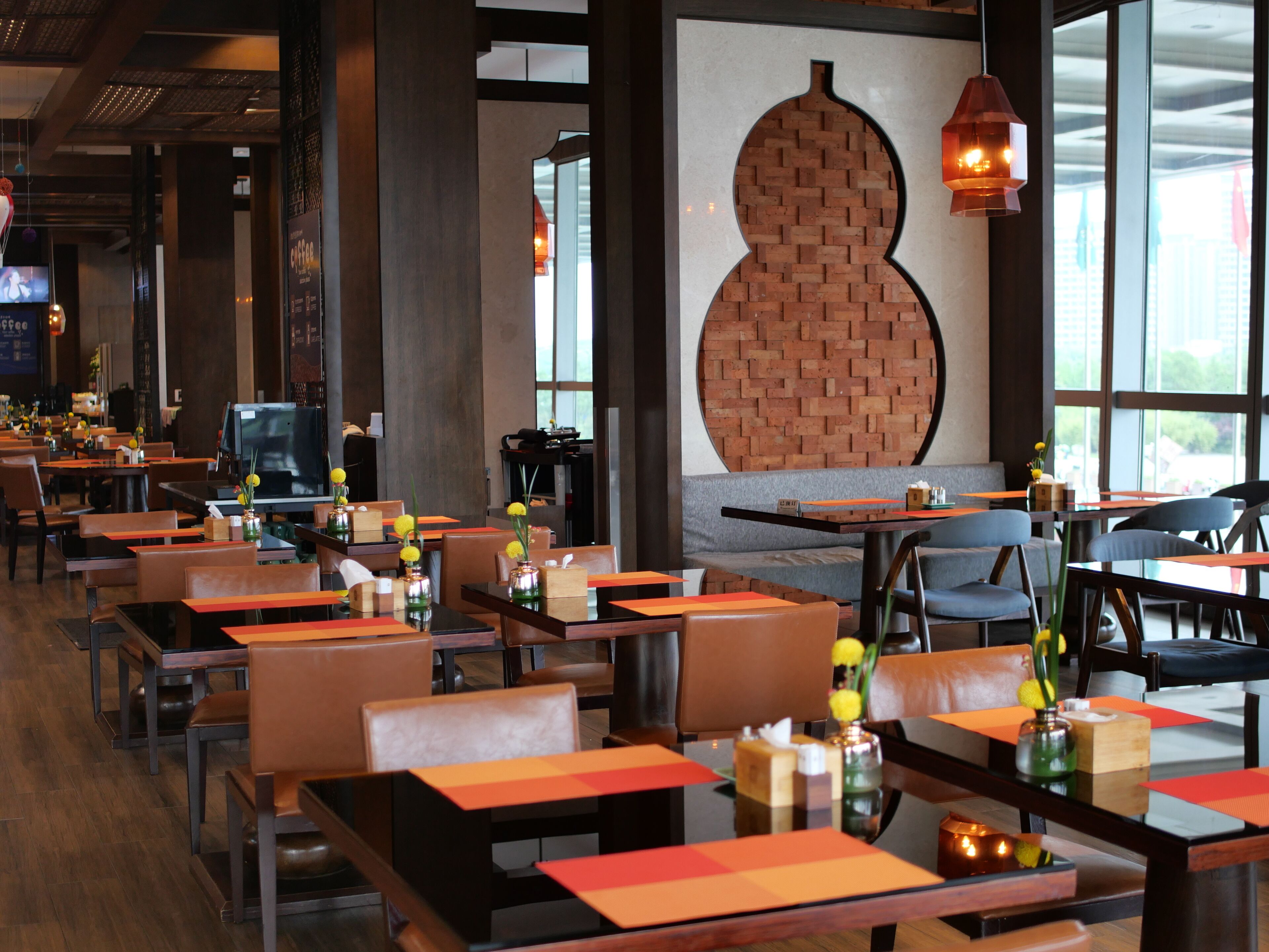 Interior de restaurante com mesas, cadeiras e uma grande parede de tijolos.