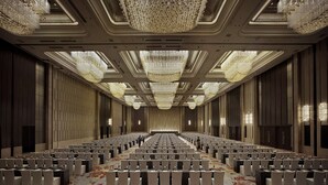 Une grande salle de conférence avec de longues rangées de tables et de chaises, des lustres somptueux et un plafond très haut.