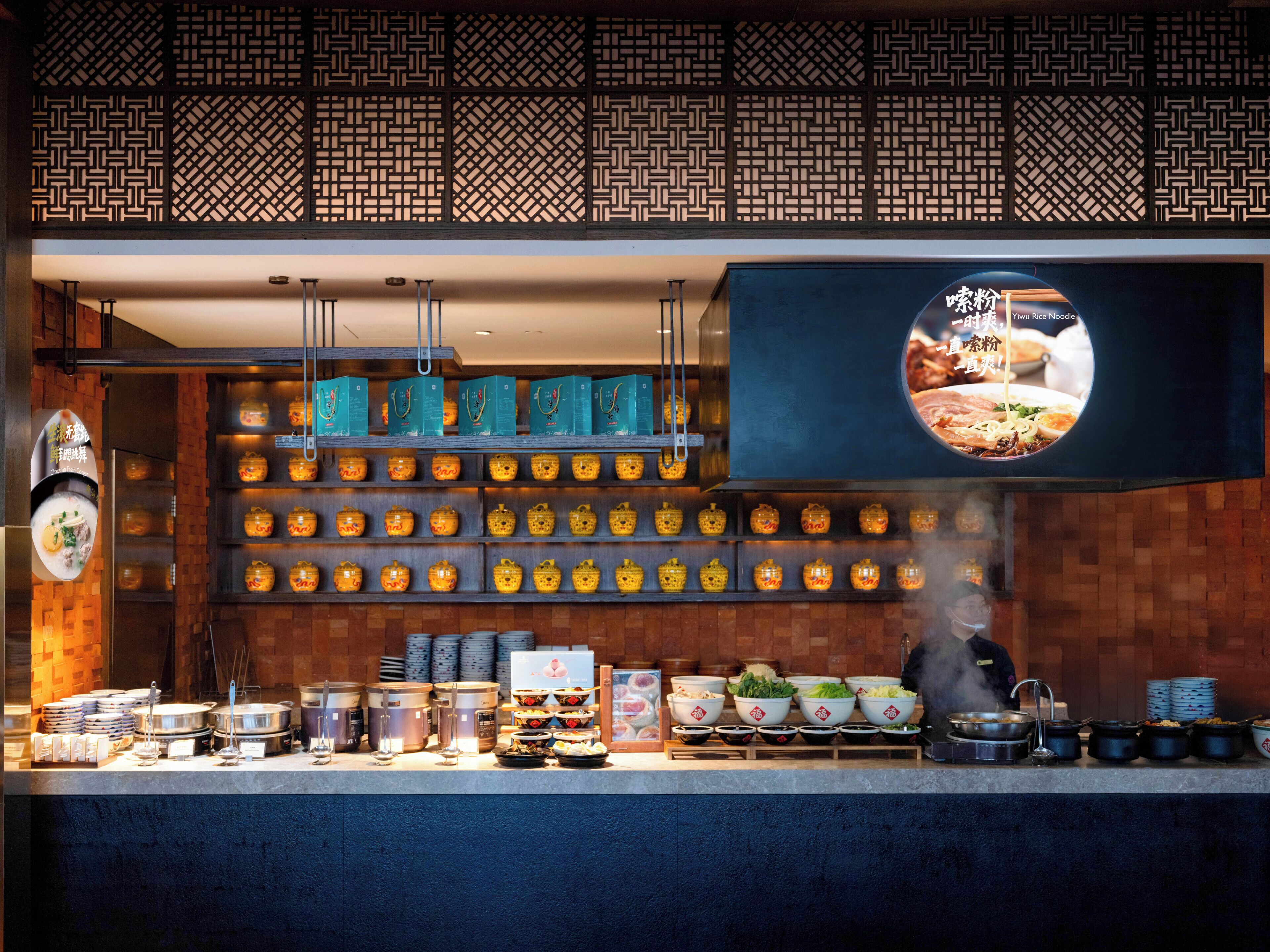 A restaurant interior with a variety of dishes displayed on shelves and counters, a hanging menu, and a steam vent.