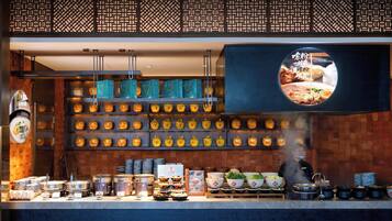 A restaurant interior with a variety of dishes displayed on shelves and counters, a hanging menu, and a steam vent.